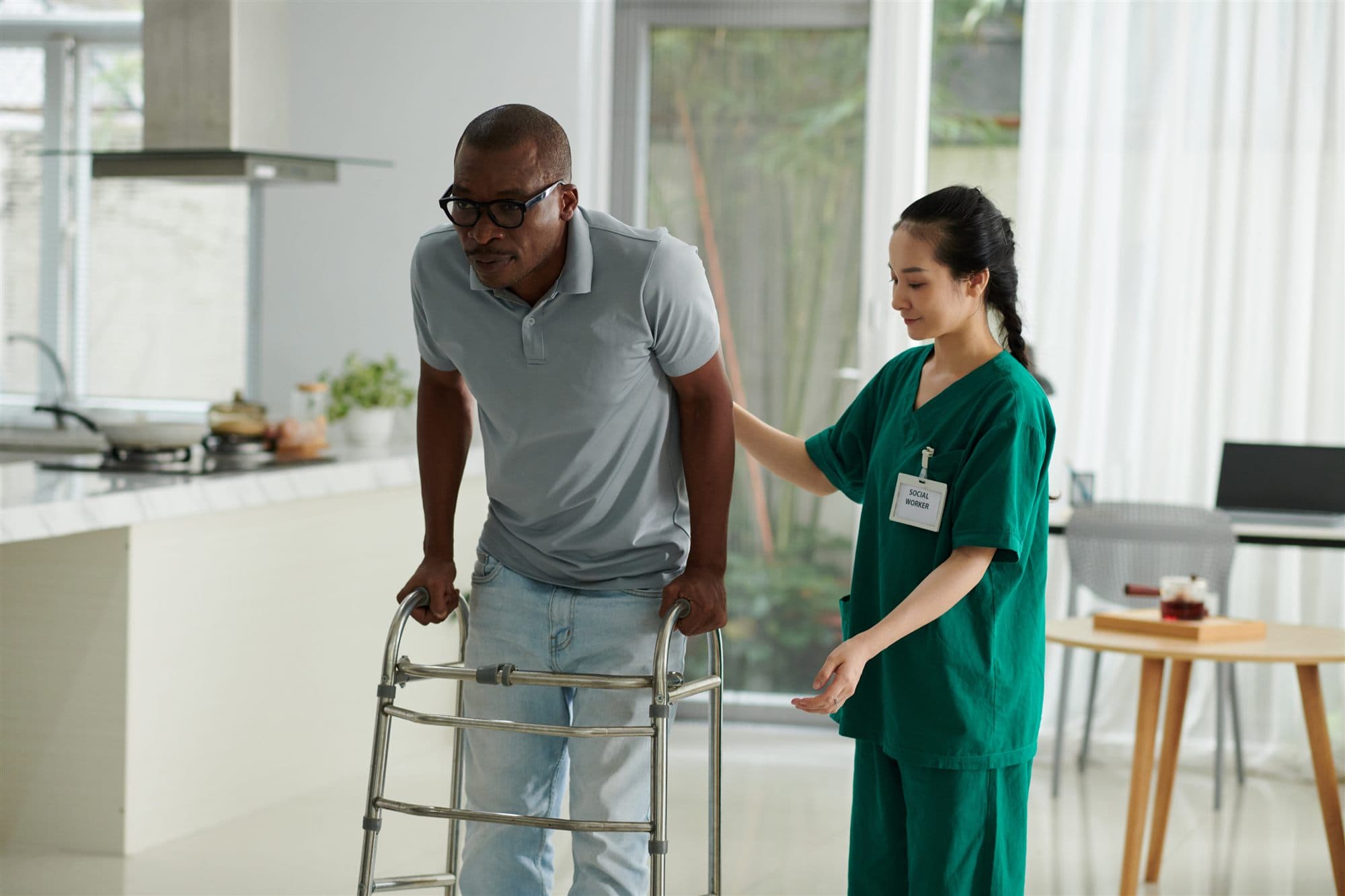A caregiver helping a man walk with a walker at home